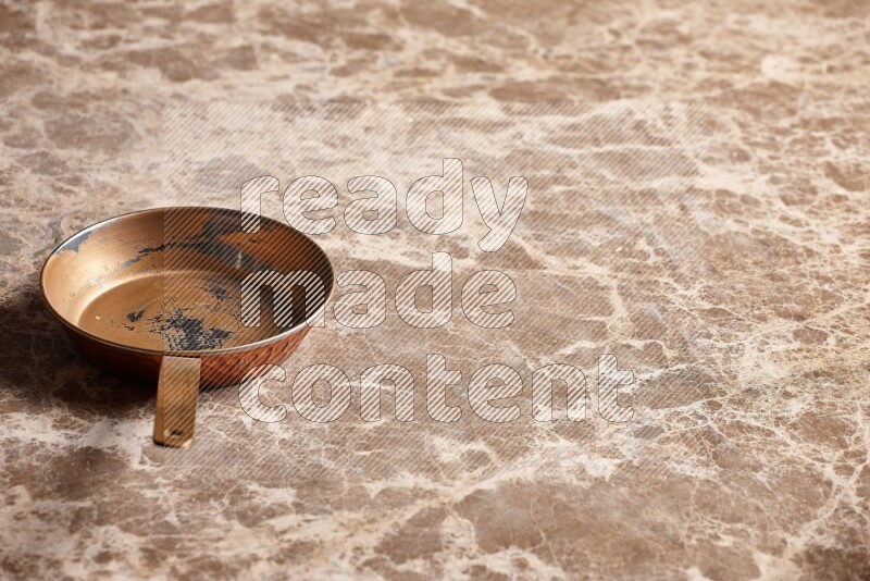 A small copper pan on beige marble background