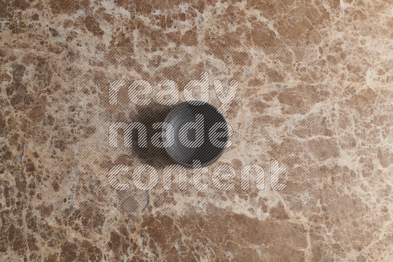 A black pottery bowl on beige marble background