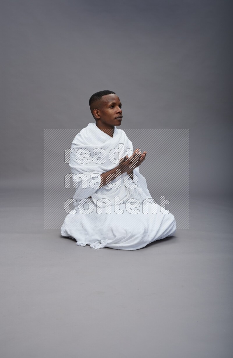 A man wearing Ehram sitting on floor dua'a on gray background
