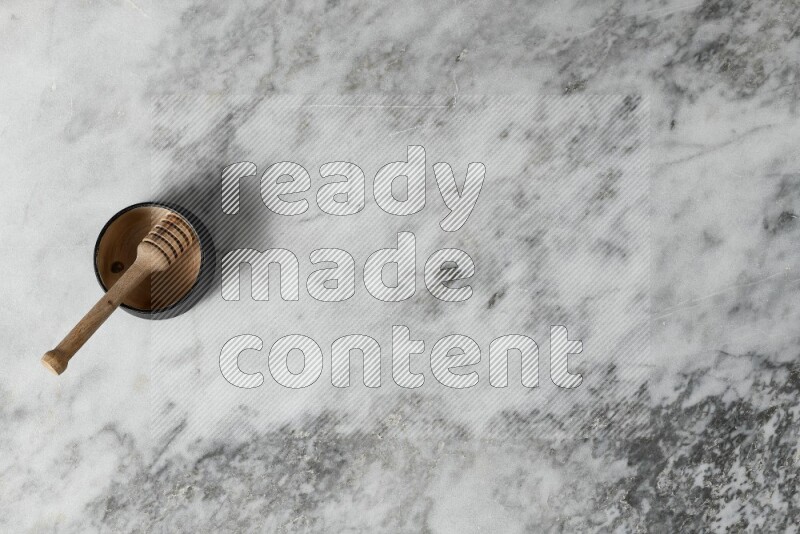 Black pottery bowl with wooden honey dipper in it on grey marble background