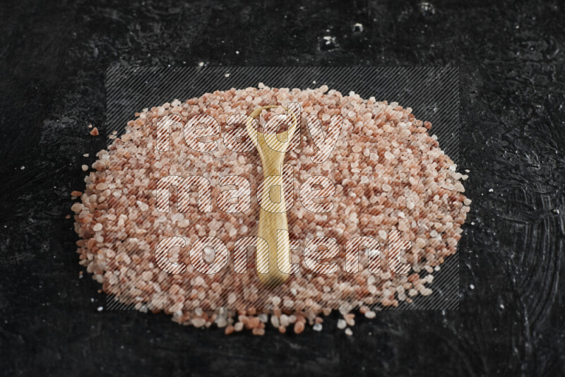 A wooden spoon full of coarse himalayan salt crystals on a bunch of the crystals on black background