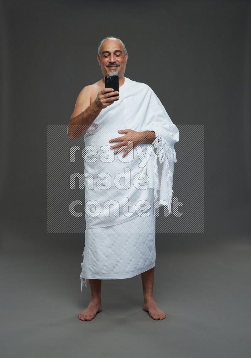 A man wearing Ehram Standing texting on phone on gray background