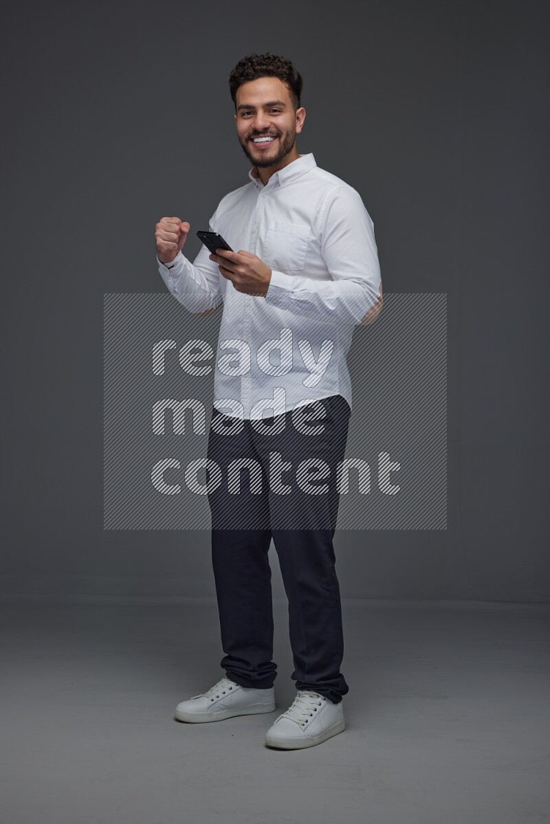 A man wearing smart casual standing and using his phone eye level on a gray background