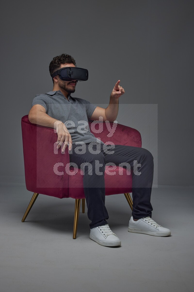A man wearing casual and wearing VR while sitting on a burgundy chair eye level on a gray background
