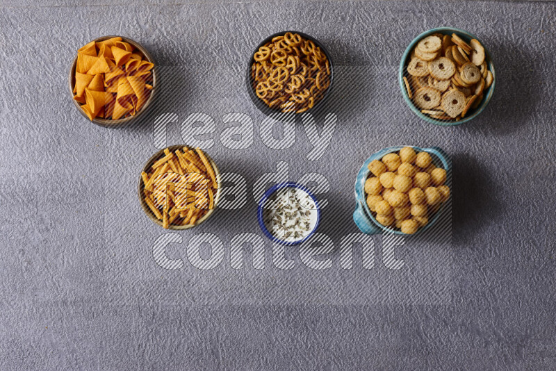 Assorted snacks in pottery bowls on grey background