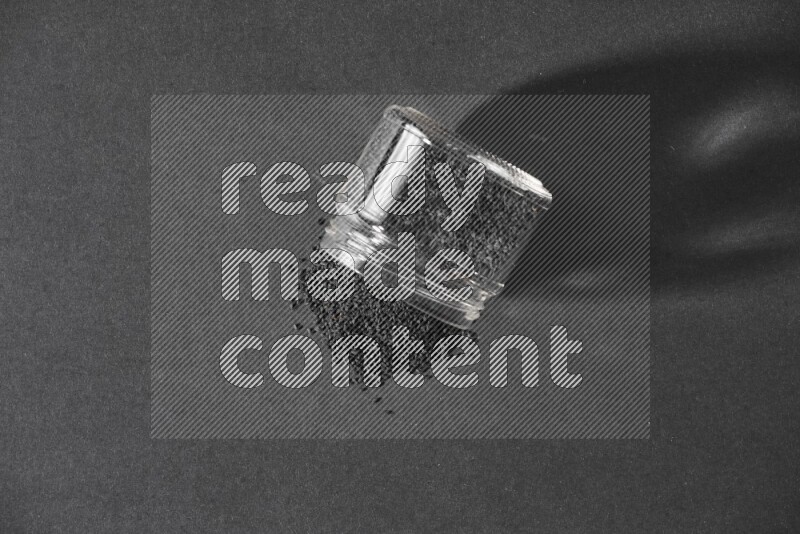 A flipped glass jar full of black seeds and the seeds spread out on a black flooring