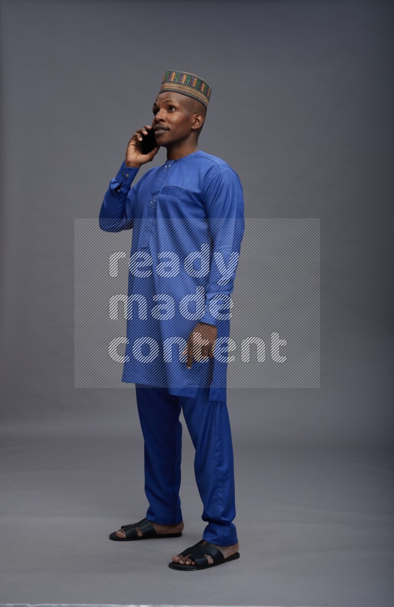Man wearing Nigerian outfit standing talking on phone on gray background