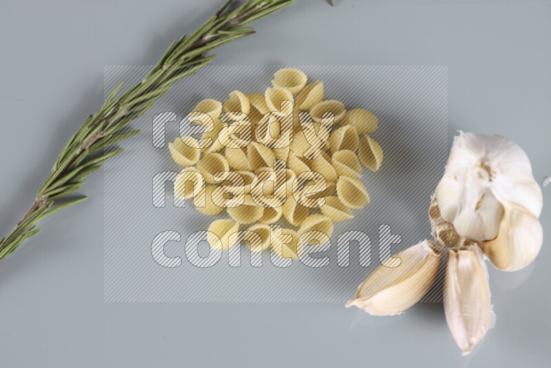 Raw pasta with different ingredients such as cherry tomatoes, garlic, onions, red chilis, black pepper, white pepper, bay laurel leaves, rosemary, cardamom and mushrooms on light blue background