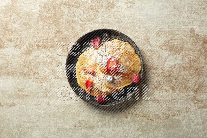 Three stacked mixed berries pancakes in a black plate on beige background