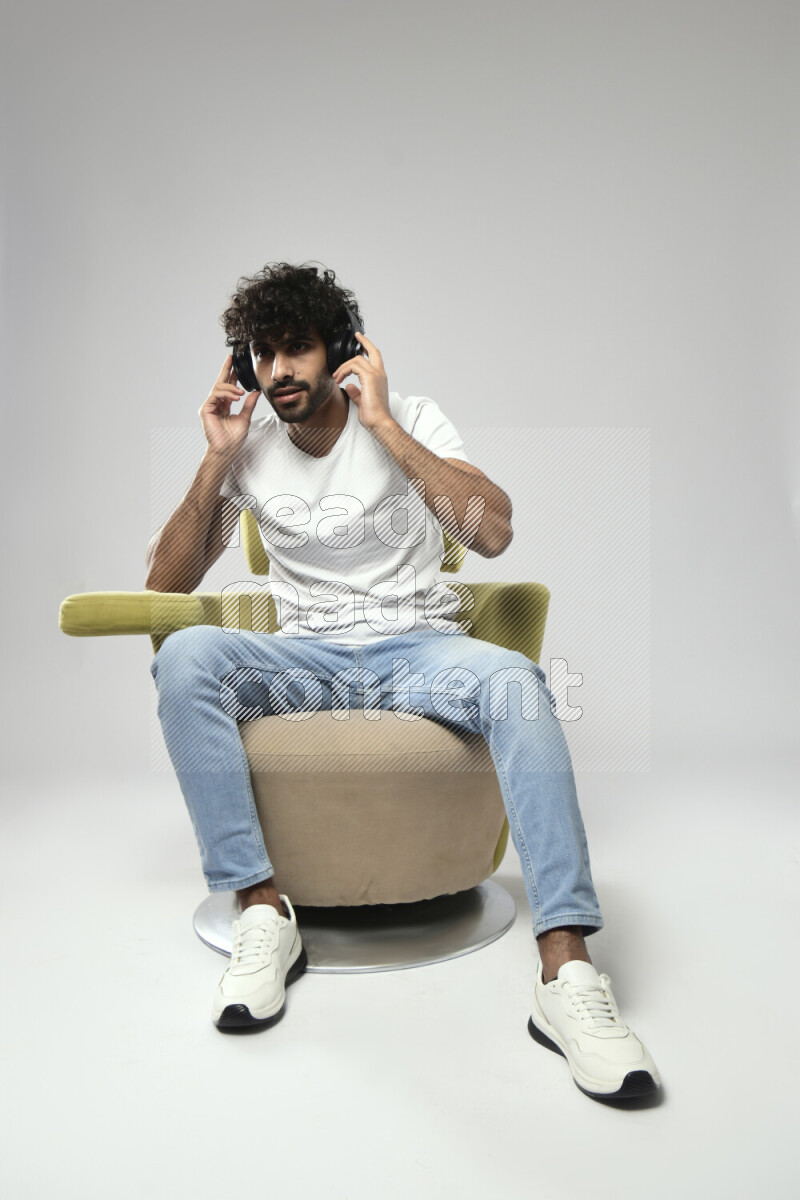 A man wearing casual sitting on a chair putting on headphones on white background