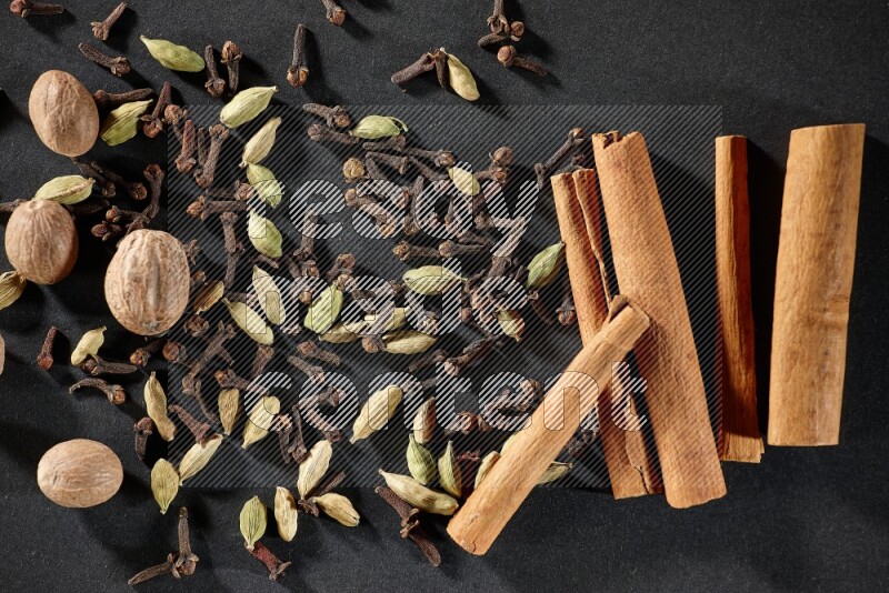 Cardamom, cloves, nutmeg and cinnamon sticks on black flooring