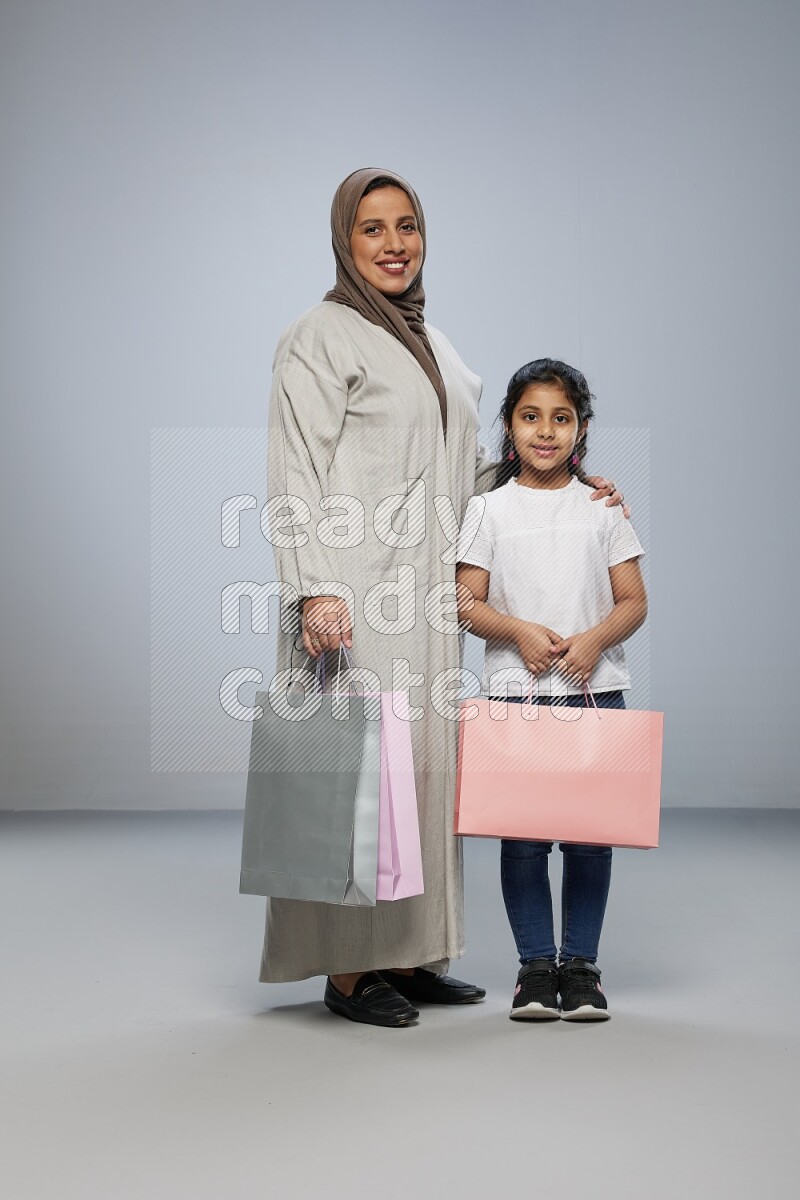 Mom and daughter holding shopping bags on gray background