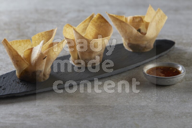 wonton cups with soy sauce ramkin on oval slate on grey textured counter top