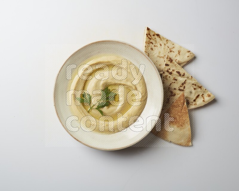 Hummus in a pottry plate garnished with parsley on a white back ground
