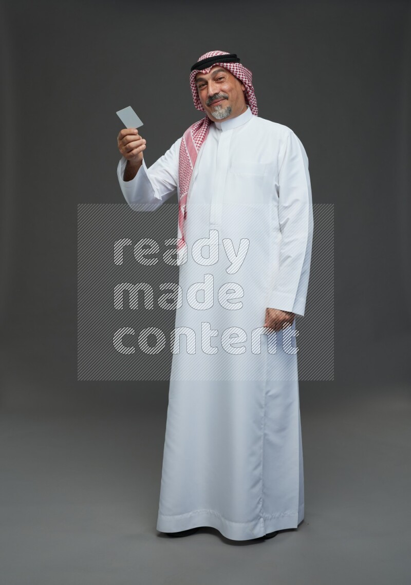 Saudi man with shomag Standing holding ATM card on gray background