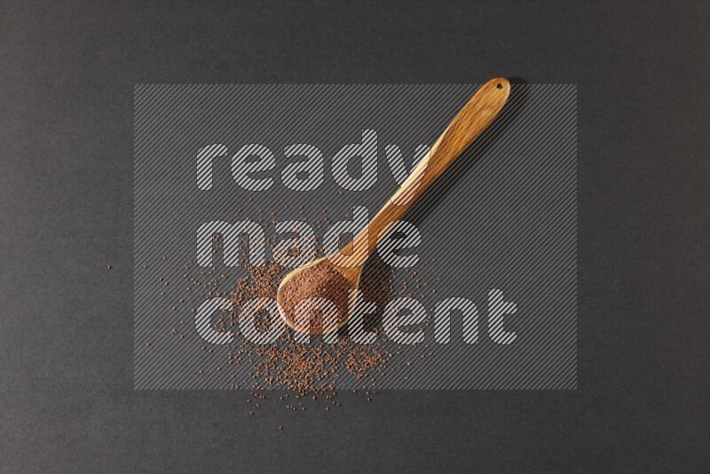 A wooden ladle full of garden cress seeds and seeds spread beside it on a black flooring