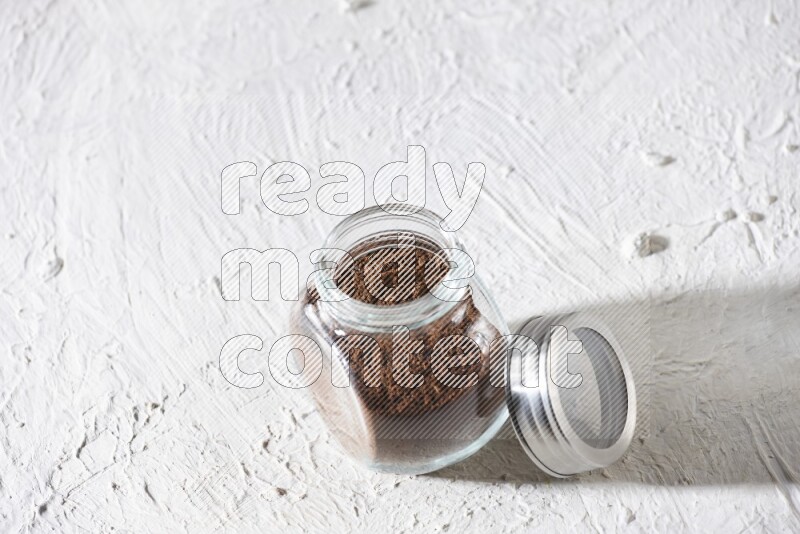 A glass spice jar full of cloves powder on textured white flooring