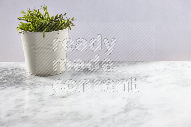 Green artificial plant in white pot on light grey marble background