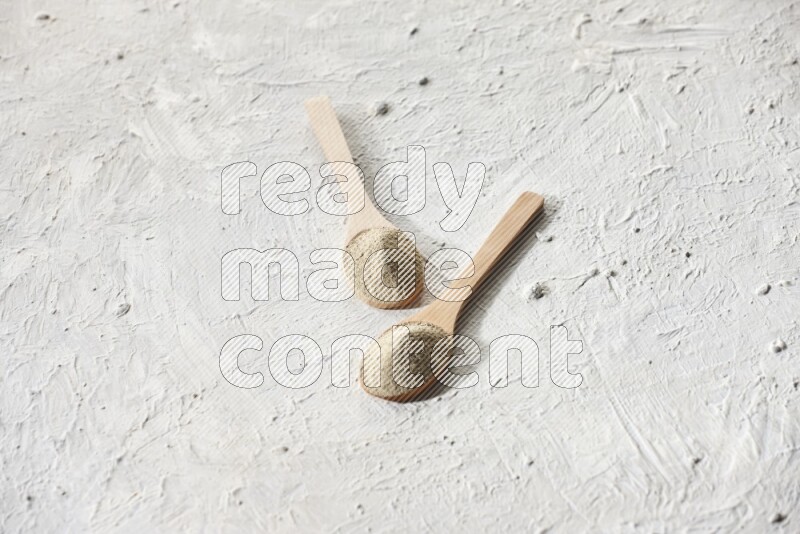 2 wooden spoons full of white pepper powder on textured white flooring