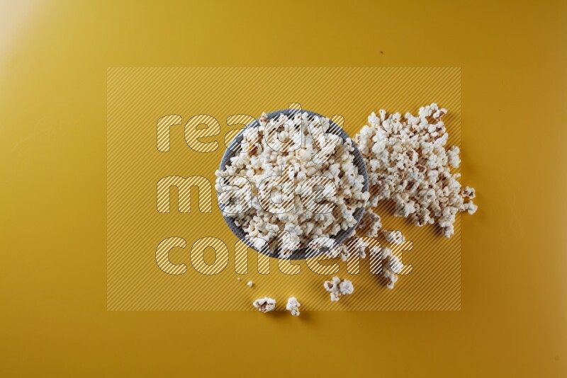 A multicolored pottery bowl full of popcorn with popcorn beside it on a yellow background in different angles
