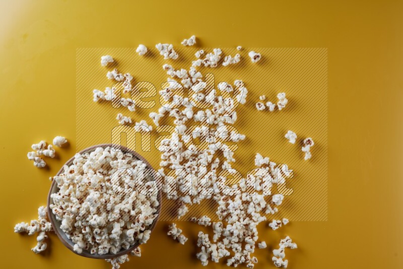 A brown pottery bowl full of popcorn with popcorn beside it on a yellow background in different angles