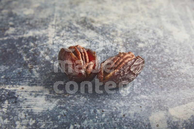 two pecan stuffed madjoul dates on a rustic blue background
