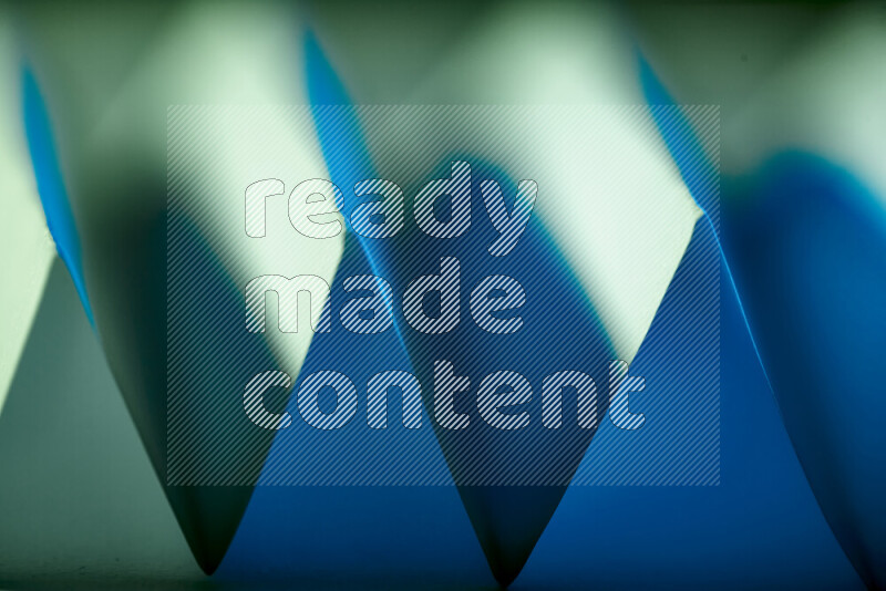 A close-up abstract image showing sharp geometric paper folds in green and blue gradients