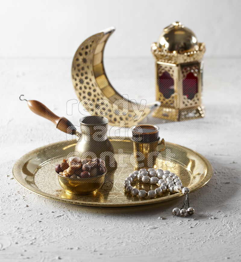Nuts in a metal bowl with coffee and prayer beads on a tray beside lanterns in a light setup