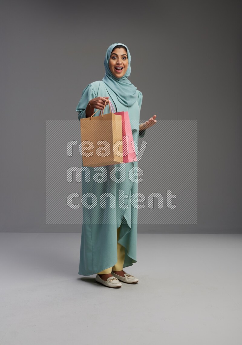 Saudi Woman wearing Abaya standing holding shopping bag on Gray background