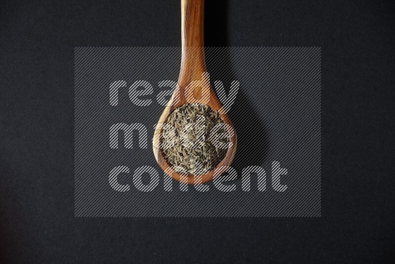 A wooden ladle full of cumin seeds on black flooring