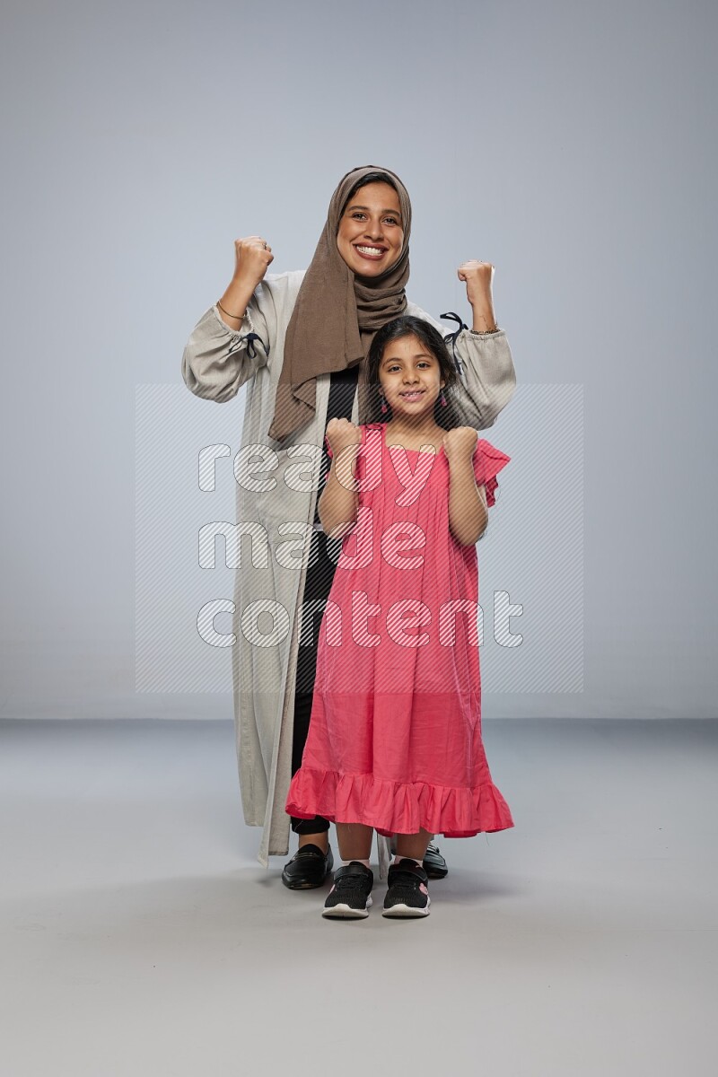 A girl and her mother interacting with the camera on gray background