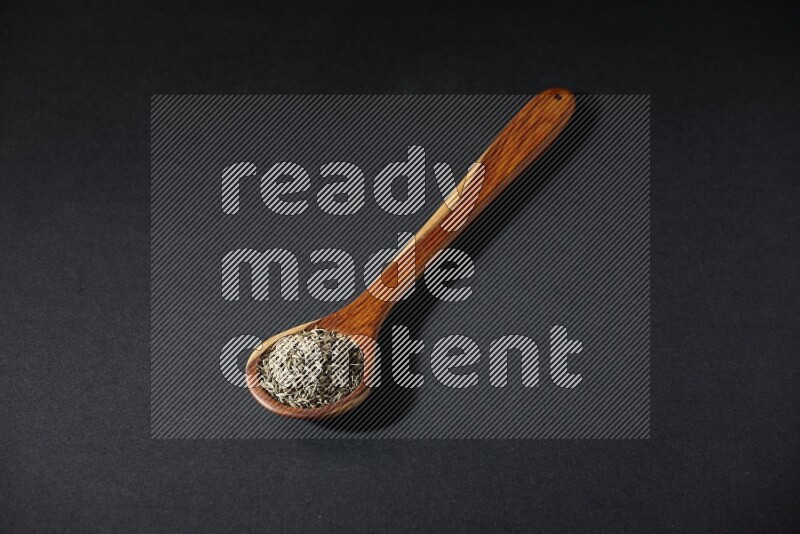 مغرفة خشبية ممتلئة بحبوب الكمون على خلفية سوداء