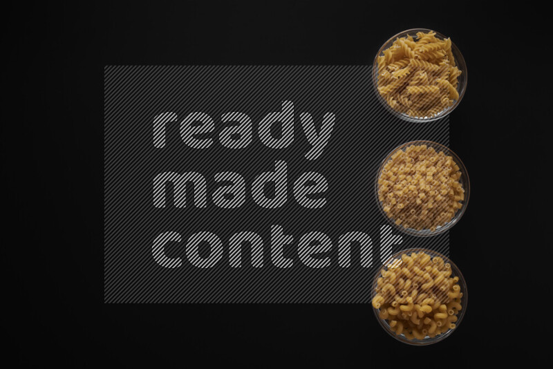 Different pasta types in 3 glass bowls on black background
