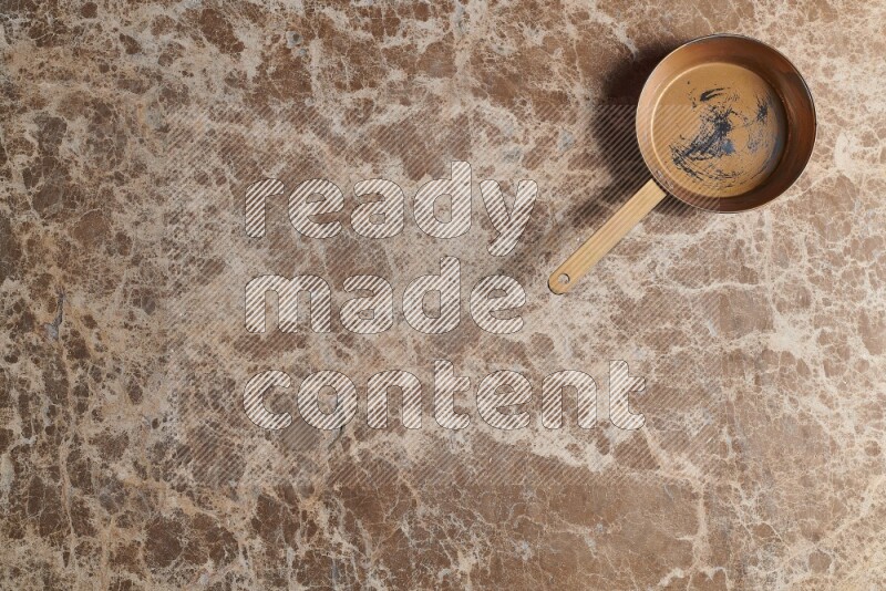 A small copper pan on beige marble background