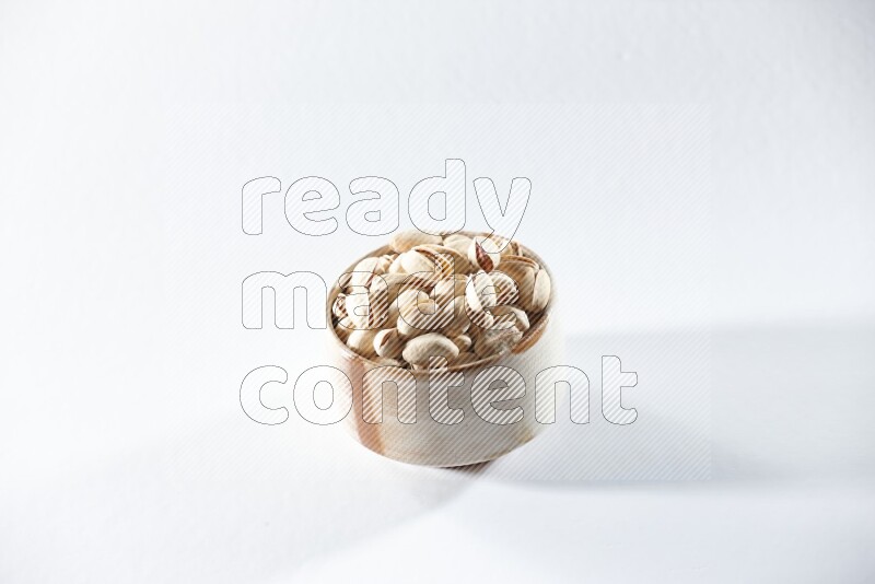 A beige ceramic bowl full of pistachios on a white background in different angles