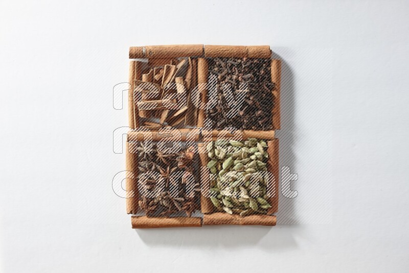 4 مربعات من أعواد القرفة ممتلئة بالهيل واليانسون النجمي والقرنفل والقرفة على أرضية بيضاء