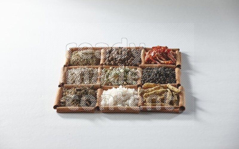 9 squares of cinnamon sticks full of cardamom in the middle surrounded by turmeric, salt, dried basil, white pepper, cumin, allspice, red dried chilis and black pepper on white flooring