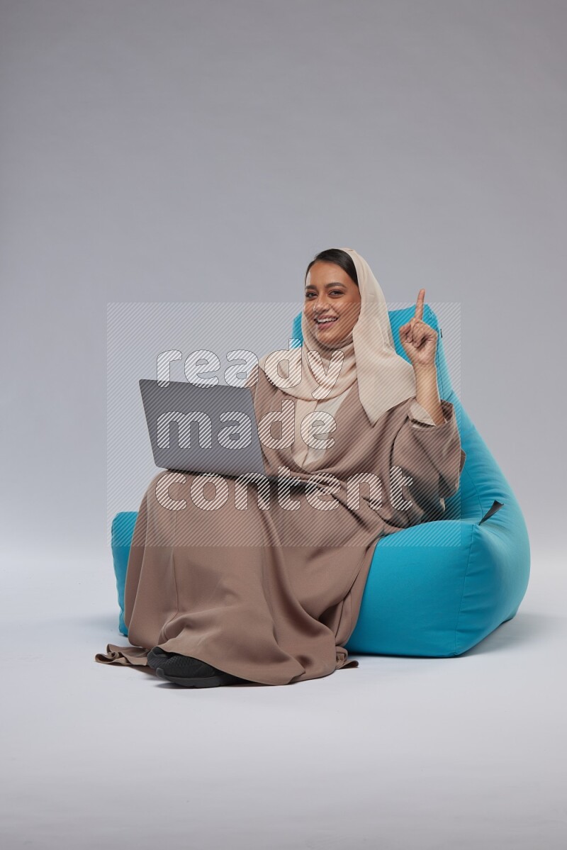 A Saudi woman sitting on a blue beanbag and working on laptop