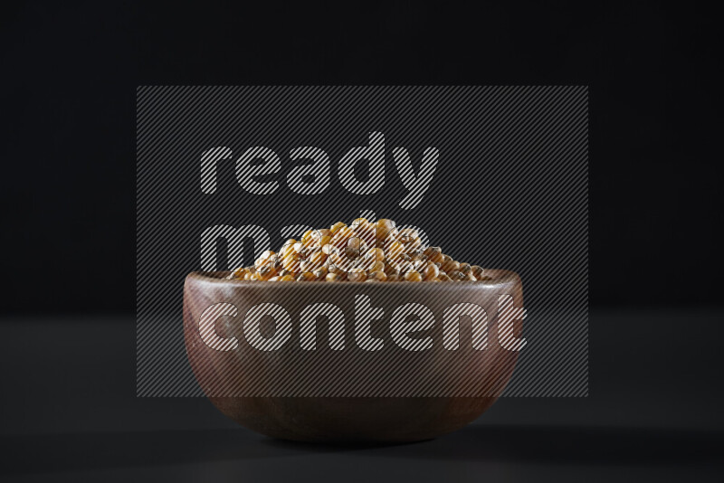 Dry corn kernels in a wooden bowl on grey background