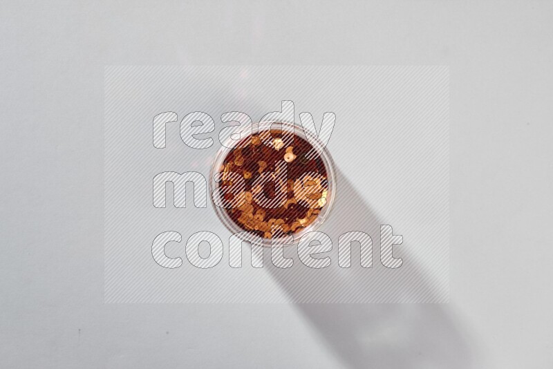 Colored flat sequins in a glass jar on grey background