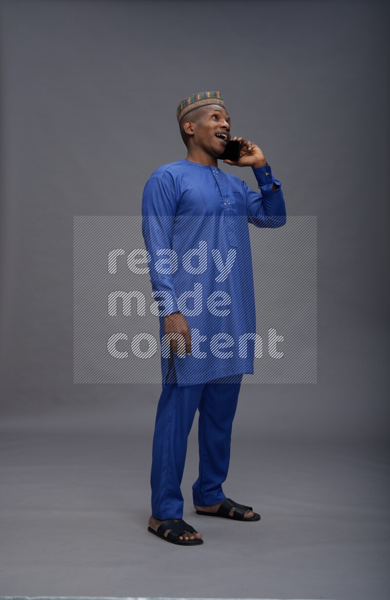 Man wearing Nigerian outfit standing talking on phone on gray background