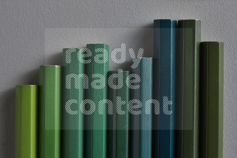 A collection of colored pencils arranged showcasing a gradient of green hues on grey background
