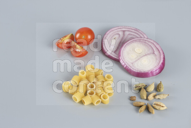 Raw pasta with different ingredients such as cherry tomatoes, garlic, onions, red chilis, black pepper, white pepper, bay laurel leaves, rosemary, cardamom and mushrooms on light blue background