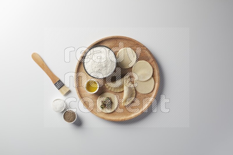 two closed sambosas and one open sambosa filled with meat while flour, salt, black pepper and oil with oil brush aside in a wooden dish on a white background