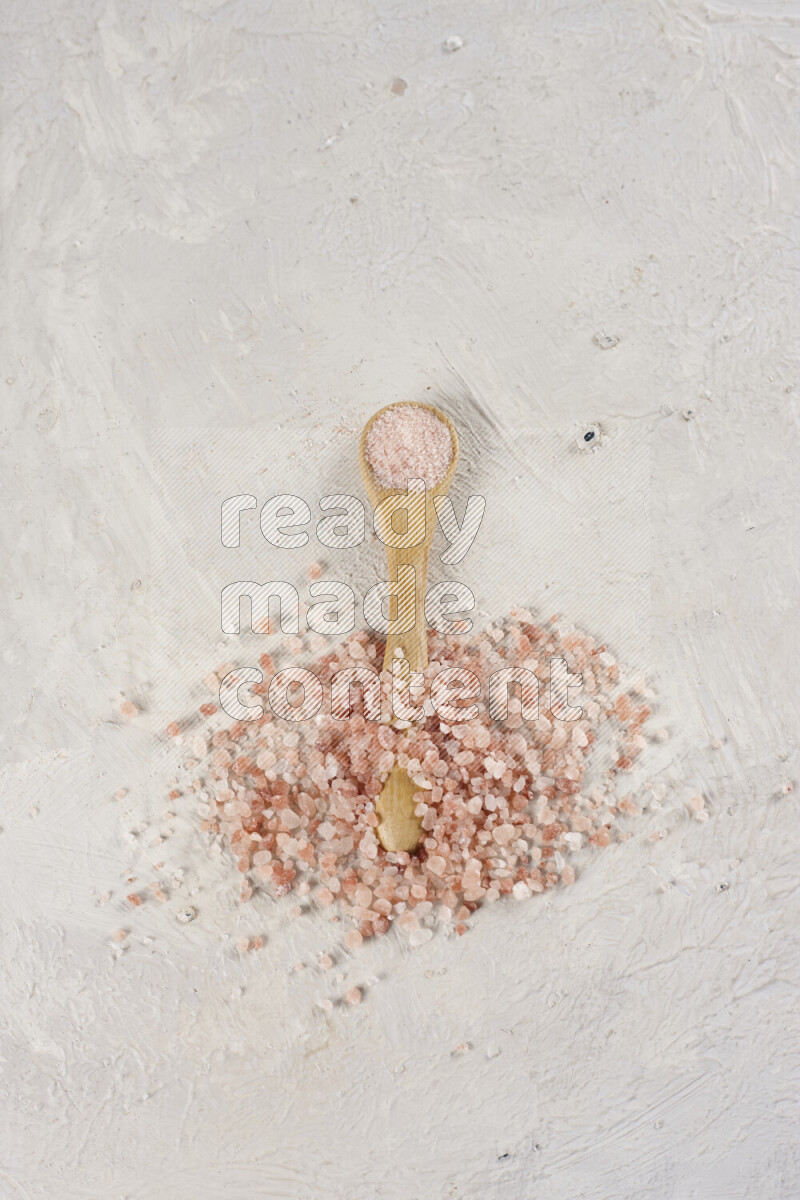 A wooden spoon full of pink himalayan salt on white background