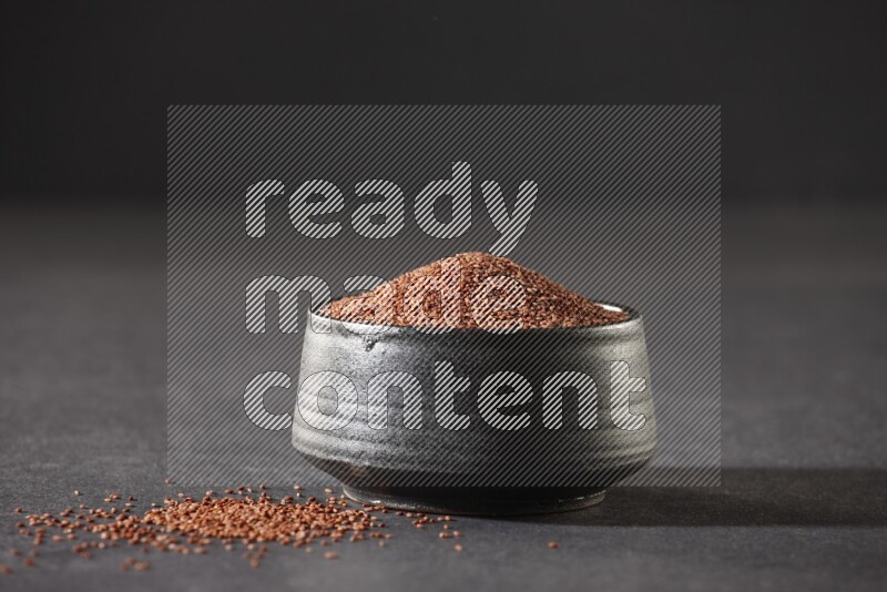A black pottery bowl full of garden cress seeds on a black flooring