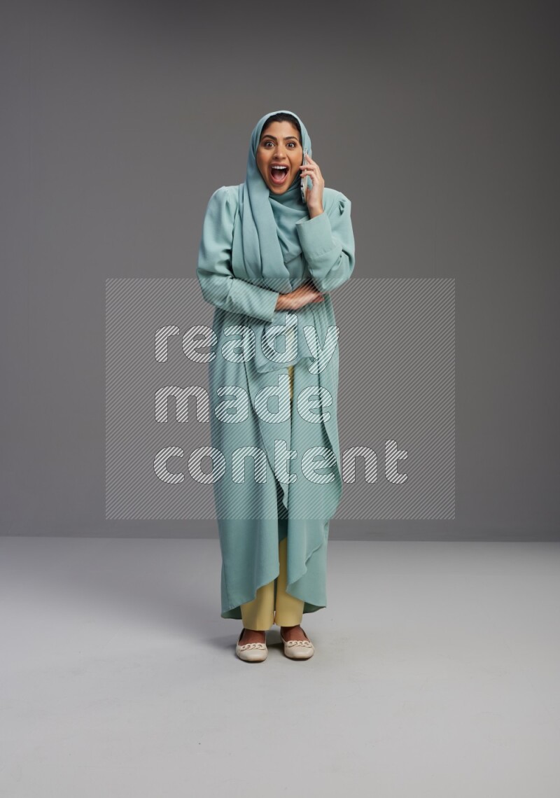 Saudi Woman wearing Abaya standing talking on phone on Gray background