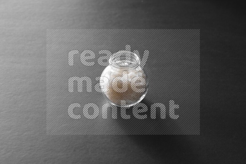 A glass spice jar full of salt on black flooring