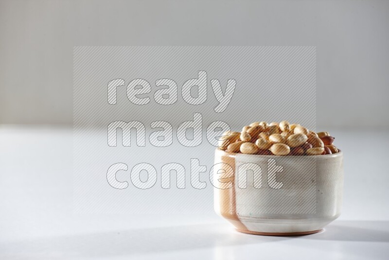 A beige ceramic bowl full of peeled peanuts on a white background in different angles