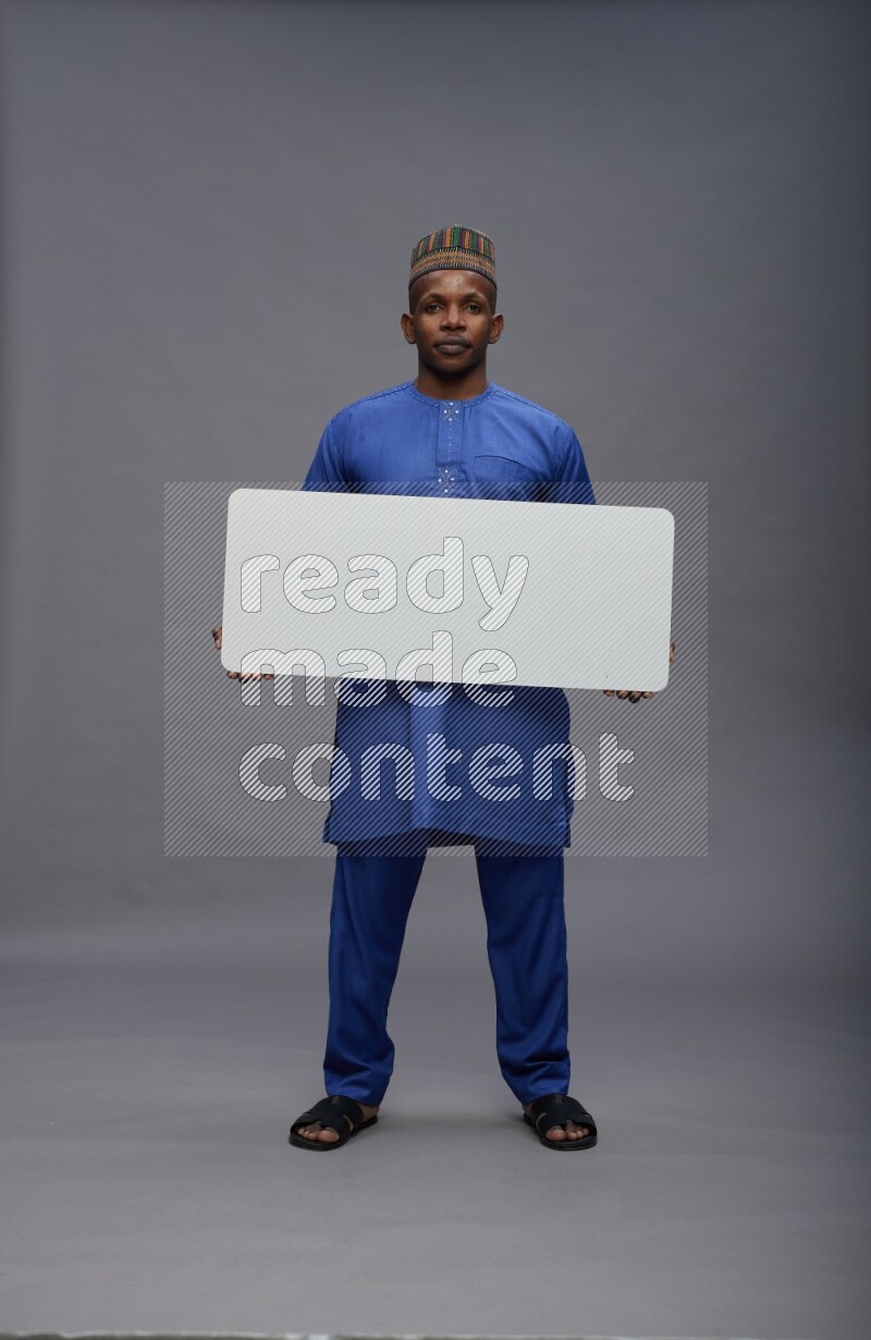 Man wearing Nigerian outfit standing holding board on gray background